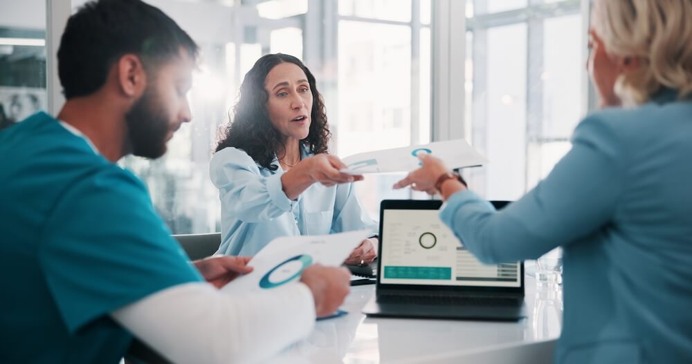 Tensed medical staff and administrators in a meeting discussing revenue issues and financial challenges in a healthcare practice.