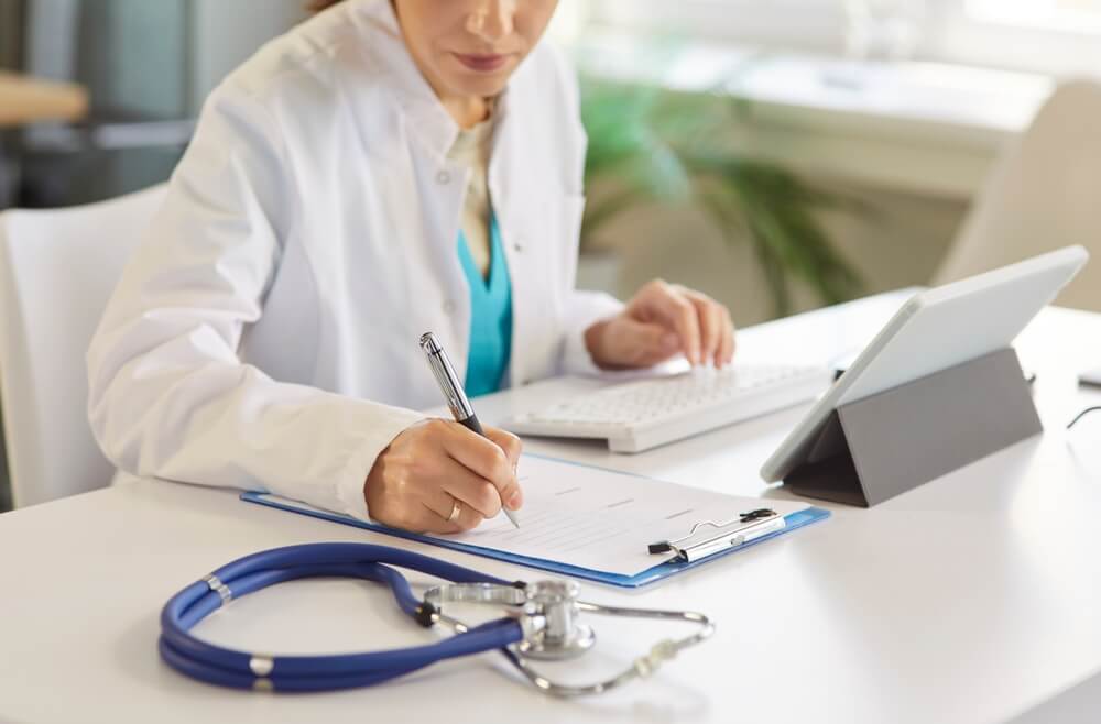 Medical scribe typing patient information into electronic health record system during physician consultation